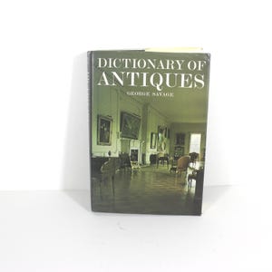 May include: A book titled "Dictionary of Antiques" by George Savage. The cover features a photograph of a room with antique furniture and a fireplace.