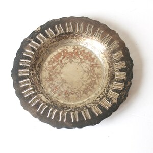 May include: A silver-plated decorative dish with a scalloped edge and an ornate design. The dish has a slightly worn appearance.