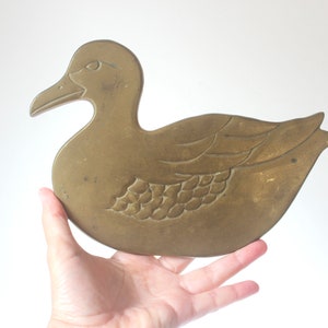 May include: A solid brass duck figurine with a detailed design. The duck is depicted in a standing position with its wings spread out.