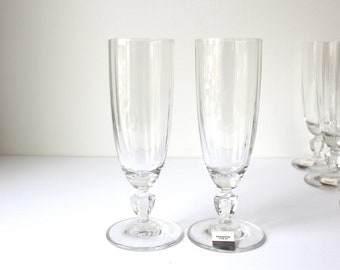 May include: Set of six clear glass champagne flutes with a fluted design and a stemmed base. The glasses are arranged in a row on a white surface.