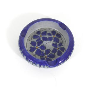 May include: A blue and white ceramic ashtray with a floral design. The ashtray has a scalloped edge and four indentations for cigarettes.