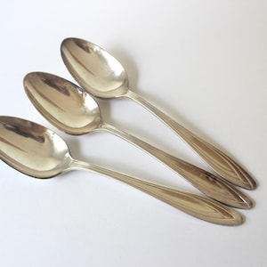 May include: Three silver spoons with ornate handles, arranged in a row on a white background.