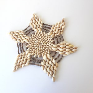 May include: A white seashell starburst wall hanging with a brown beaded border.