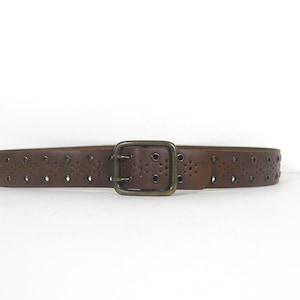 May include: A brown leather belt with a brass buckle and a decorative pattern of small holes. The belt has a double-prong buckle.