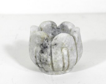 May include: A white marble lotus flower candle holder with gray veining. The holder is carved with intricate details and has a round base.