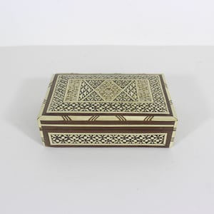 May include: A small wooden box with intricate inlaid geometric patterns in shades of brown and white. The box has a hinged lid and is made of wood.