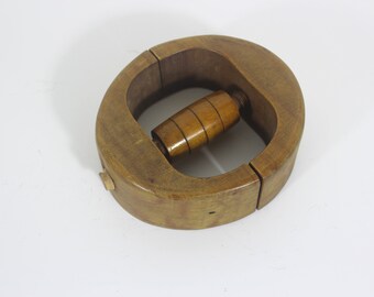 May include: A wooden hat form with a round, oval shape. The form is made of two pieces that are hinged together. There is a wooden roller in the centre of the form.