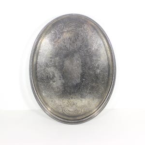 May include: A silver oval serving tray with an ornate embossed design. The tray has a beaded edge.