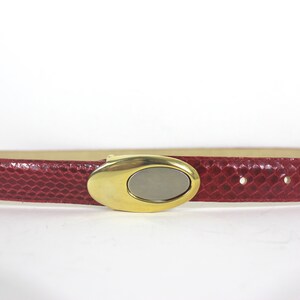 May include: A red leather belt with a gold oval buckle. The buckle has a silver oval insert.