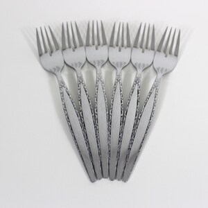 May include: A collection of seven silver forks arranged in a fan shape. Each fork has a decorative handle and four tines. The forks are set against a white background, creating a clean and elegant presentation.