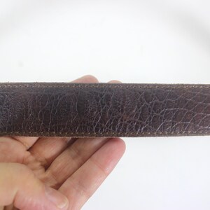 May include: A close-up of a brown leather belt with a stitched edge.