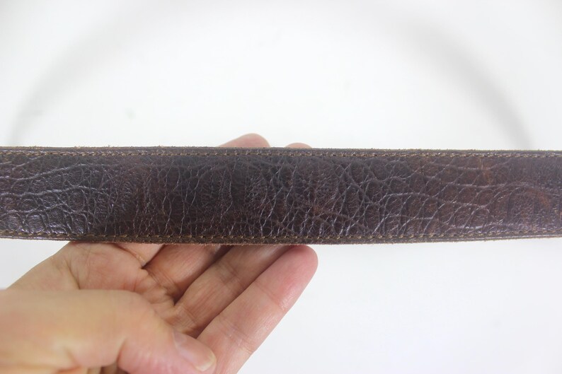 May include: A close-up of a brown leather belt with a stitched edge.