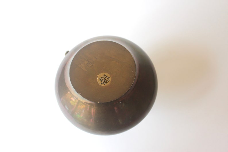 Pode incluir: Um vaso redondo de lat&atilde;o maci&ccedil;o com acabamento dourado. A parte inferior do vaso tem um adesivo que diz "Solid Brass Made in India".