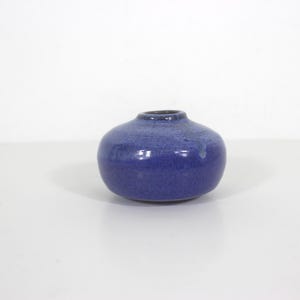 May include: A small, round, blue ceramic vase with a narrow neck. The vase has a textured surface and a glossy finish, reflecting light. The colour is a deep, saturated blue, suitable for home decor.