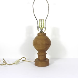 May include: A wooden table lamp with a brown, round base and a simple metal shade. The lamp has a cord with an inline switch.