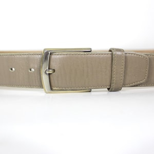 May include: A taupe leather belt with a silver-toned rectangular buckle. The belt has a classic design with a single belt loop and several holes for adjustment. The belt is approximately 3.2 cm wide.