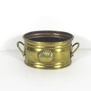 May include: A brass planter with two handles and a shell design. The planter is round and has a copper interior.