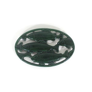 May include: Dark green oval trivet with a design of four fish. The trivet is made of cast iron and is designed to protect surfaces from hot cookware. A decorative kitchen accessory.