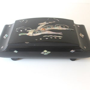 May include: A black wooden box with a hinged lid decorated with a mother-of-pearl inlay of three deer running. The box has four small feet and a diamond pattern on the sides.