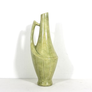 May include: A green ceramic vase with a unique, curved design and a handle. The vase has a textured surface and vertical lines.