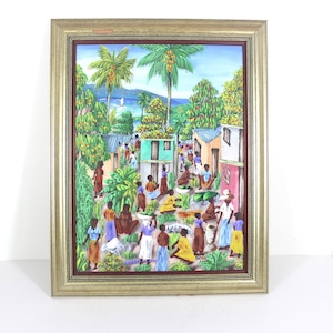 May include: A framed painting depicting a colorful scene of a Caribbean village with palm trees, houses, and people in the street. The painting is set against a backdrop of a blue ocean and a green mountain.