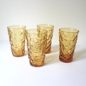 May include: Four amber glass tumblers with a textured, raised design. The glasses are empty and sitting on a white surface.