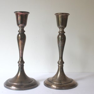 May include: Two silver candle holders with a classic design. The holders have a wide base and a tall, slender stem.