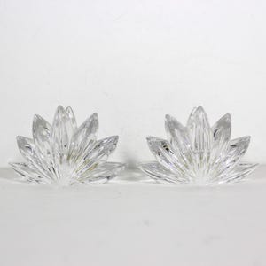May include: A pair of clear crystal candle holders shaped like lotus flowers. The holders are made of faceted glass and have a delicate, elegant design.