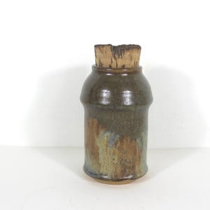 May include: A brown ceramic jar with a cork lid. The jar has a mottled glaze with shades of brown, green, and blue.