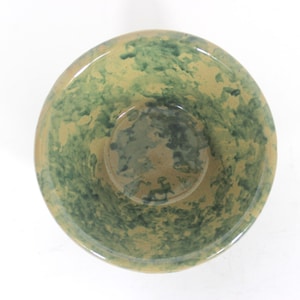 Peut inclure: Un bol en céramique avec un glaçage tacheté vert et beige. Le bol a une forme arrondie avec un centre légèrement surélevé. Les surfaces intérieures et extérieures sont recouvertes d'un motif moucheté, créant un aspect unique et organique.
