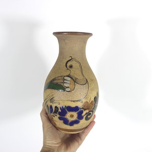 May include: A brown ceramic vase featuring a bird and floral design. The bird is painted in shades of green, white, and brown. The flowers are painted in shades of blue, green, and brown.