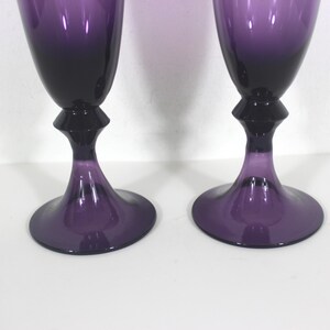 May include: Two purple glass goblets with a flared base and a stem with a decorative design.