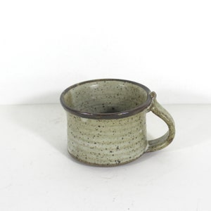 Peut inclure: Une tasse en céramique de couleur brun clair mouchetée avec un bord brun foncé et une anse.
