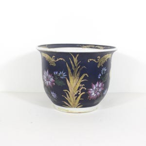 May include: A small, blue ceramic planter with gold and floral accents. The planter has a round shape and a wide rim.