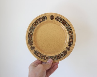 May include: A beige ceramic plate with a brown and black geometric pattern around the rim.
