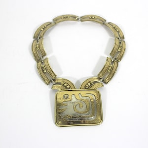 May include: A gold necklace with a square pendant featuring a geometric design in silver and gold.