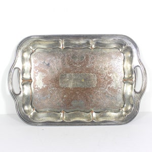 Peut inclure: Un plateau de service en argent avec des motifs gravés ornés et deux poignées. Le plateau est rectangulaire avec des coins arrondis et un bord légèrement surélevé.