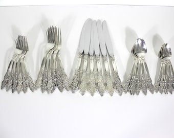 May include: A set of silverware with ornate designs, including forks, knives, and spoons. The silverware is arranged in rows on a white surface.