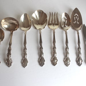 May include: A set of eight silver-plated serving utensils, including a ladle, a serving spoon, a slotted spoon, a serving fork, a slotted serving spoon, a cake server, a butter knife, and a sugar spoon.