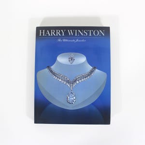 Peut inclure: Publicité bleue pour les bijoux Harry Winston. L'image présente un collier et une bague en diamants exposés sur un mannequin. Le collier a un grand pendentif en diamant en forme de poire. Le texte "HARRY WINSTON" est en haut.