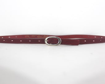 May include: A burgundy leather belt with a silver oval buckle. The belt has small holes for adjusting the size.