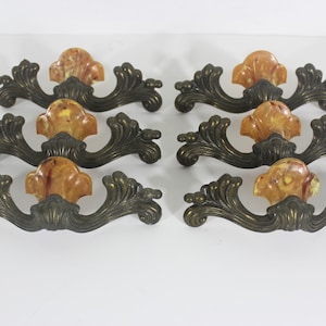 May include: Eight antique cabinet knobs with ornate brass scrollwork and yellow-brown marbled plastic centres.
