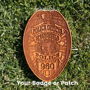 May include: A wooden police badge with the text "POLICE OFFICER SPRINGFIELD" and the number "960" carved into it. The badge is oval-shaped and features an eagle at the top. The text "Your Badge or Patch" is at the bottom.