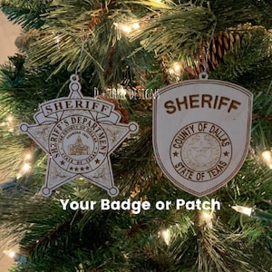 May include: Two wooden Sheriff badges hang on a Christmas tree. One is a star shape, the other a shield. Both are engraved with "Sheriff" and "County of Dallas, State of Texas". The text "Your Badge or Patch" is below.