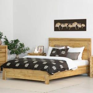 May include: A wooden bed frame with a matching headboard and a black and white patterned comforter. The bed is in a bedroom with a wooden dresser and a painting on the wall. The room is decorated with plants and candles.