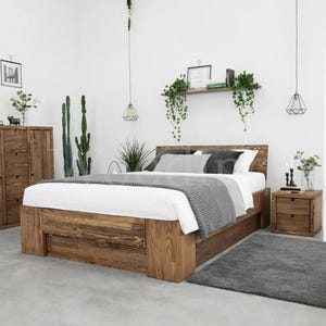 Può includere: Un letto in legno con testiera e comodino abbinati. Il letto è in legno marrone chiaro e ha un piumino bianco e una coperta grigia. La stanza ha un design moderno con piante e un tappeto grigio.
