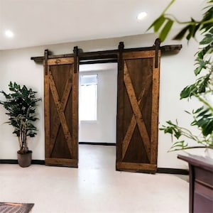 May include: A pair of brown wooden barn doors with an X-shaped design, sliding on a metal track. The doors are open, revealing a white room with a window.