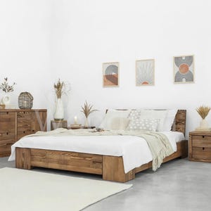 Puede incluir: Una cama de madera rústica de perfil bajo, combinada con mesitas de noche y una cómoda a juego. La cama tiene un acabado de madera natural y está cubierta con ropa de cama blanca y cojines decorativos. La habitación está decorada con arte enmarcado y plantas secas.