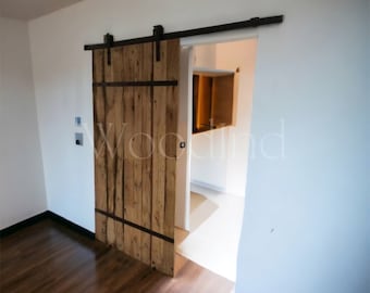 May include: A rustic wooden sliding barn door with black metal hardware, installed in a room with light brown hardwood floors.