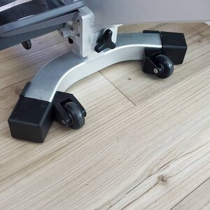 Puede incluir: Una máquina de ejercicio de plata con ruedas negras y un asiento acolchado negro. La máquina está en un suelo de madera clara.